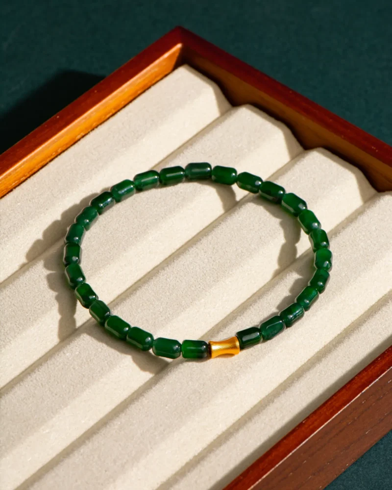 The Deep Green Feicui Bracelet, featuring drum-shaped beads and a warm-tone spacer, is displayed on a beige, ridged jewelry tray inside a wooden box.