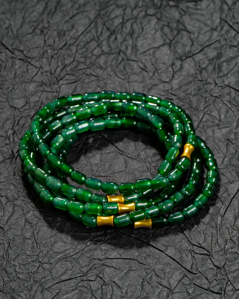 A coil of deep green glass beads with small gold accents, arranged in a stacked bracelet, rests on a textured black surface.