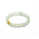 A jade bead bracelet with round, pale green beads and a single small gold accent piece, displayed on a white background.