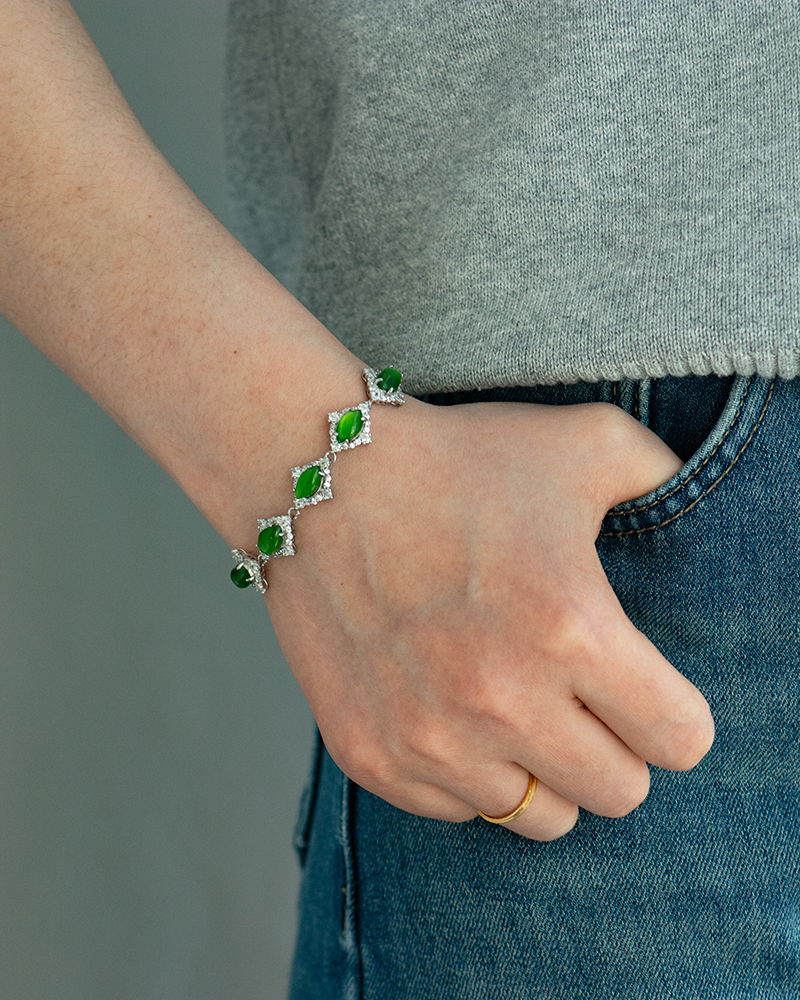 LYU_5655 A person wearing a gray top and blue jeans has their hand in their pocket, showing a gold ring and a silver bracelet with green gemstones and surrounding white stones on their wrist.