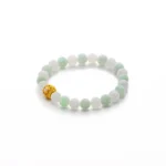 A beaded bracelet with alternating light green and white jade beads, featuring a single gold filigree bead, displayed on a white background.