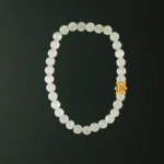 A white beaded bracelet with translucent oval beads and a single decorative gold charm, displayed against a solid black background.