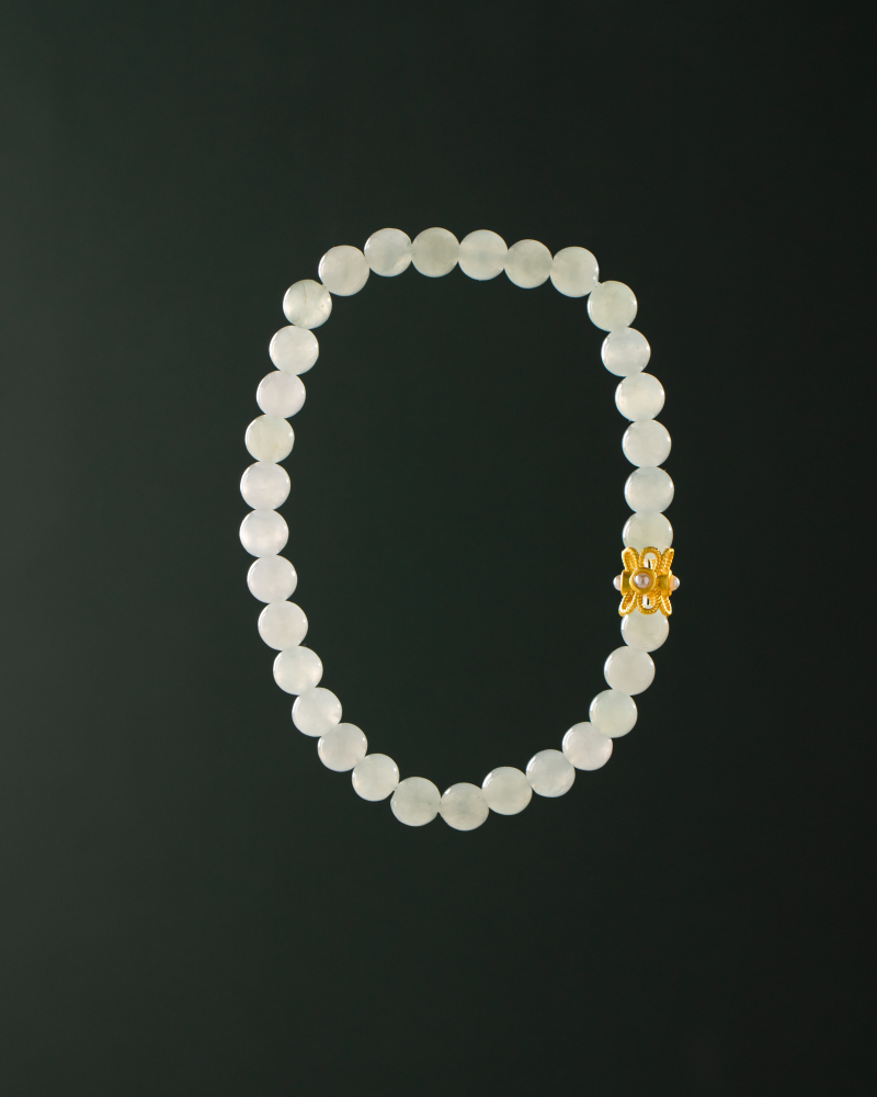 A white beaded bracelet with translucent oval beads and a single decorative gold charm, displayed against a solid black background.