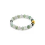 A beaded bracelet made of round, light green and white jade stones, featuring one gold bead with intricate detailing, arranged in a circle on a white background.