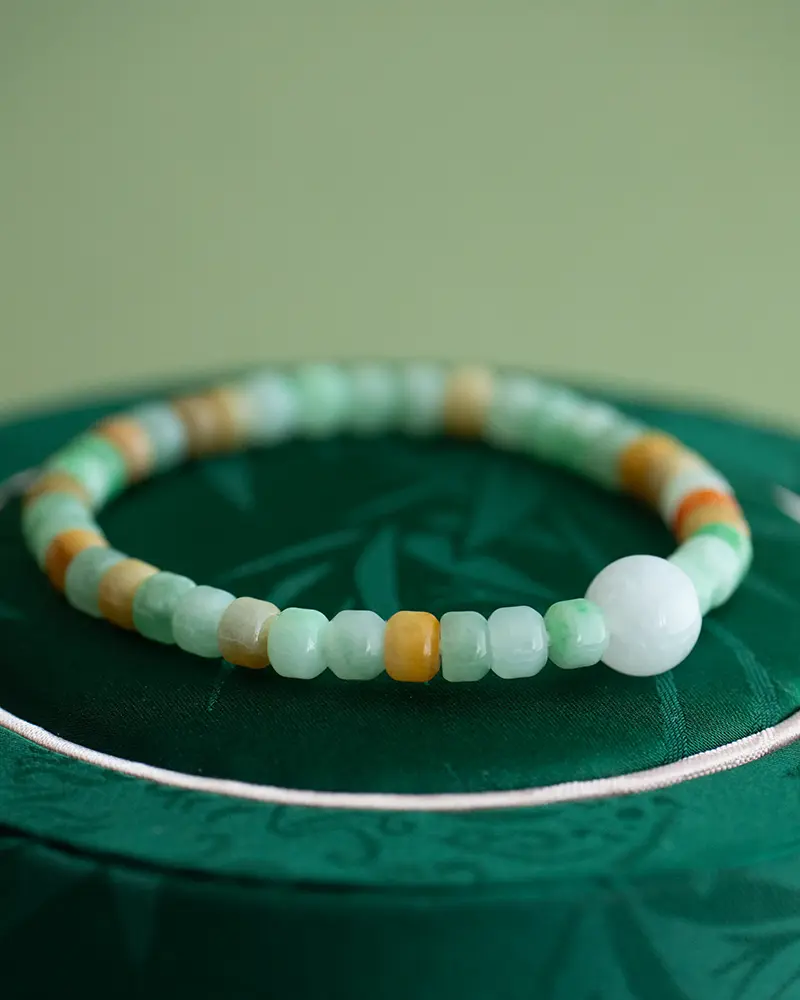 DSC_0537 拷贝 A beaded bracelet with green, white, and amber-colored stones rests on a dark green, textured surface with a soft, blurred green background.