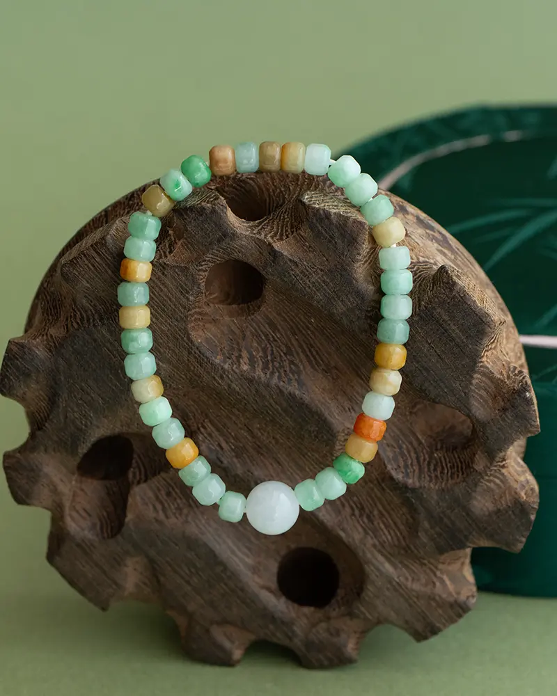 DSC_0550 拷贝 A beaded bracelet with light green, yellow, orange, and white round beads is displayed on a carved wooden stand against a green background.