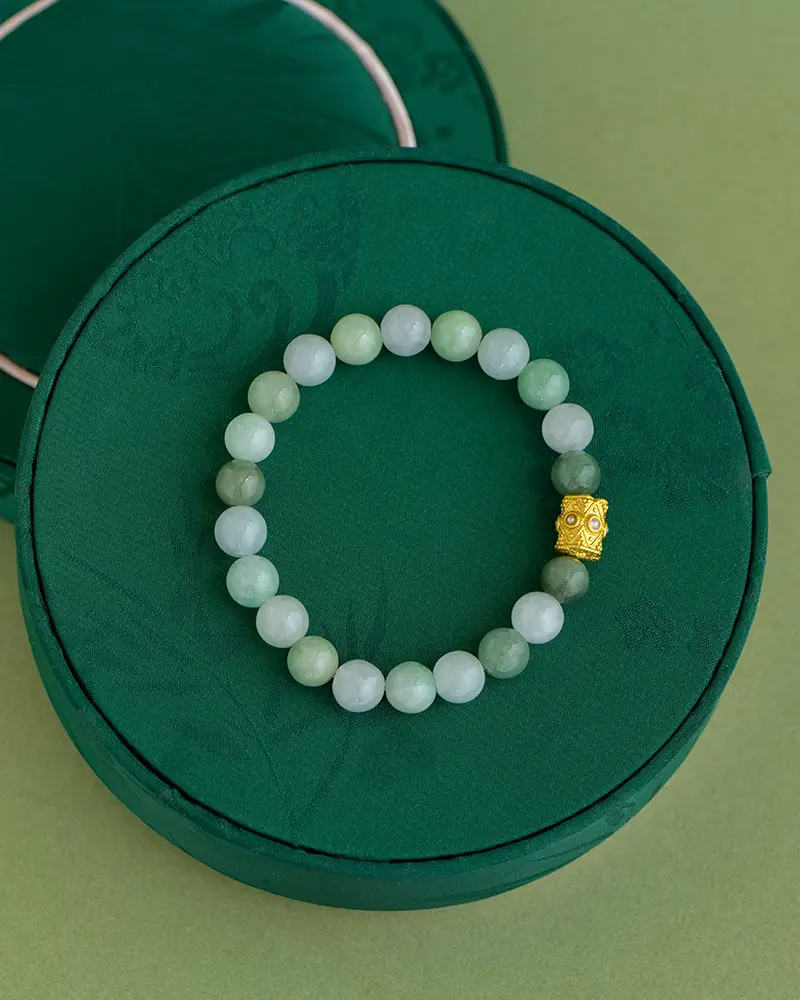 DSC_0551 拷贝 A green beaded bracelet with a single gold decorative bead is displayed on a round, dark green textured box, set against a light green background.