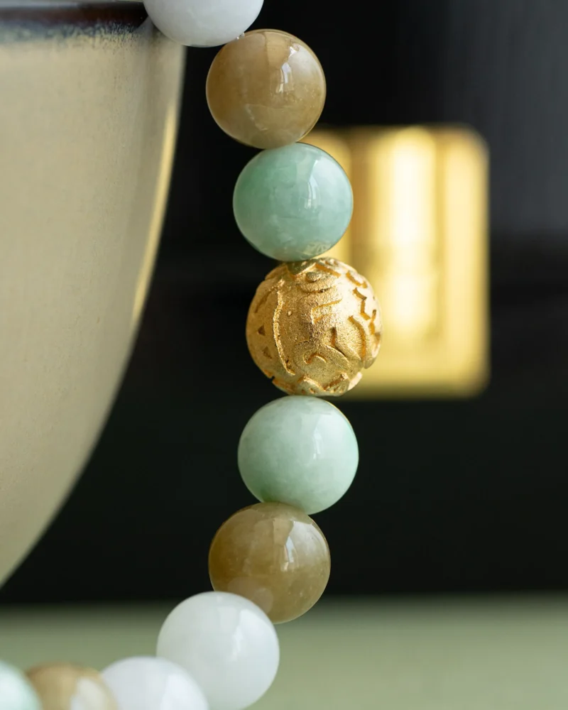 Close-up of the Light Green, White, and Brownish Yellow Jadeite Bead Bracelet — Spherical Beads with Gold-Tone Accent, draped over the edge of a ceramic bowl.