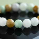 A close-up of a beaded bracelet featuring smooth round beads in shades of white, green, and brown, displayed on a glossy black surface.