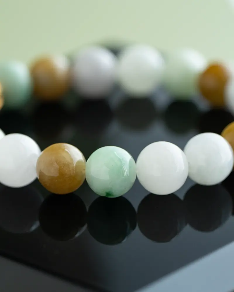 DSC_0556 拷贝 A close-up of a beaded bracelet featuring smooth round beads in shades of white, green, and brown, displayed on a glossy black surface.