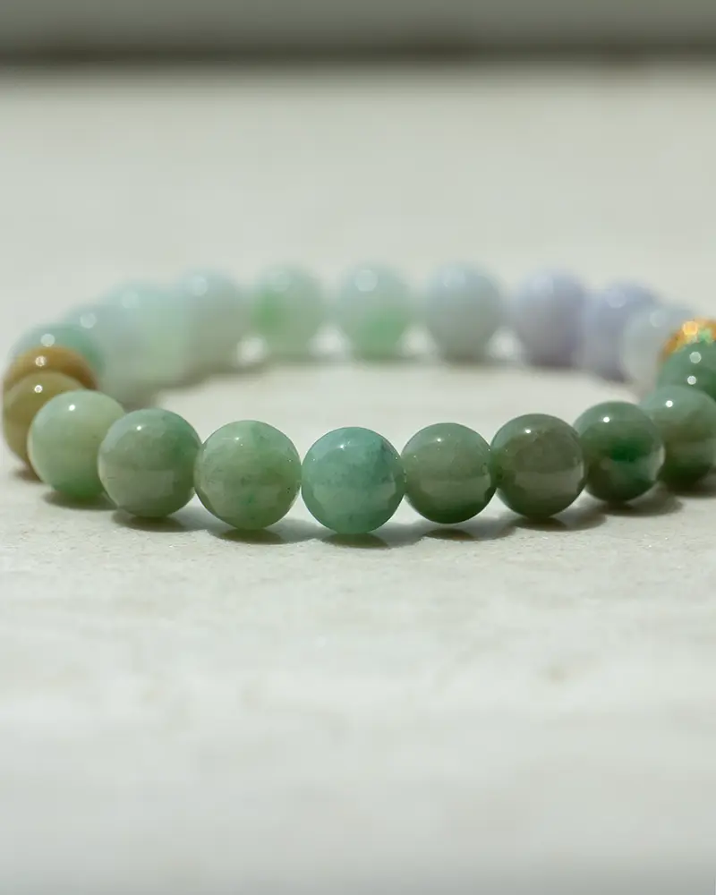 DSC_0567 拷贝 A close-up view of a beaded bracelet made of round, polished green and light-colored stones, resting on a light, textured surface.