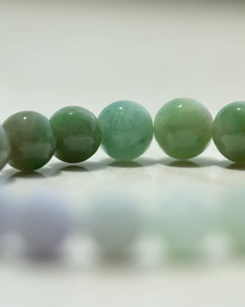 DSC_0568 拷贝 A close-up of a row of polished green jade beads, with a blurred row of lighter-colored beads in the foreground on a light surface.