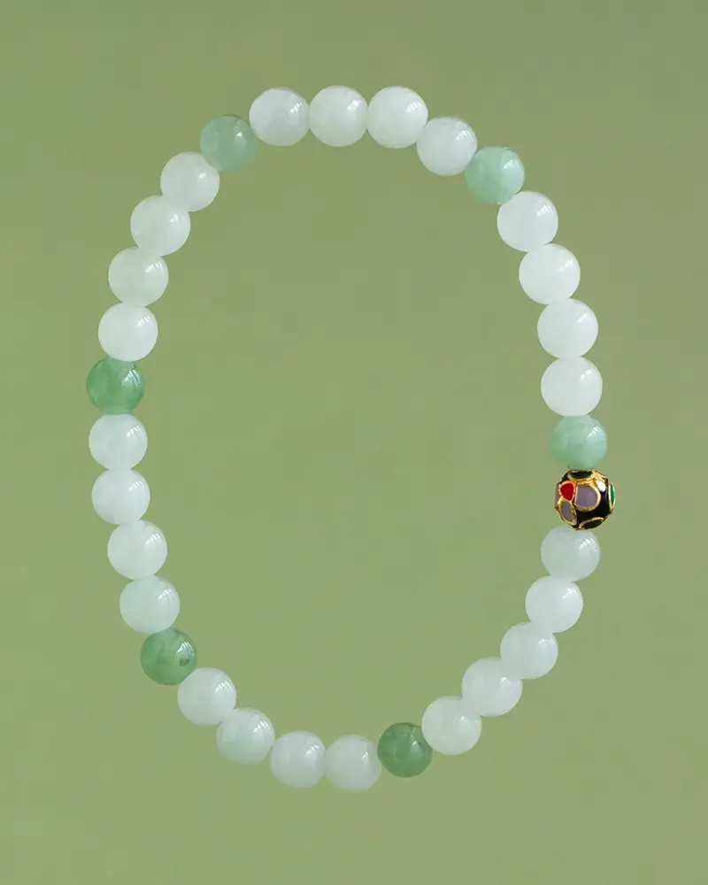 DSC_0577 拷贝 A beaded bracelet made of alternating white and light green round beads, with a single decorative bead featuring gold and red accents, displayed on a light green background.