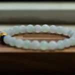 A translucent beaded bracelet made of light green stones rests on a wooden surface, with a blurred background.