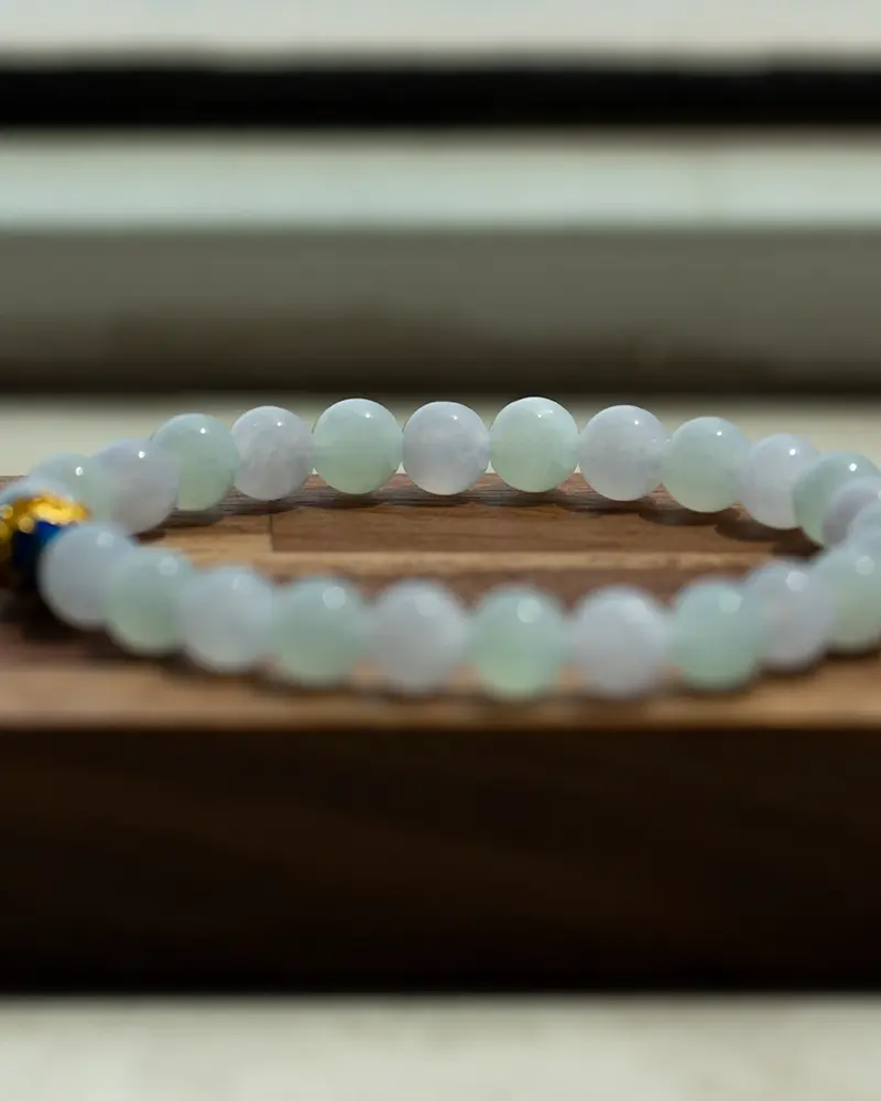 DSC_0589 拷贝 A translucent beaded bracelet made of light green stones rests on a wooden surface, with a blurred background.