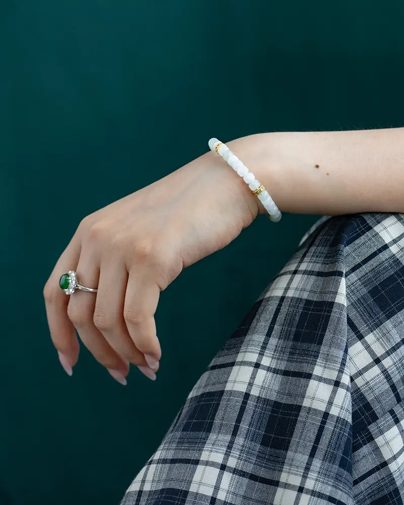DSC_0635 拷贝 A hand wearing a jade and gold bracelet and a green gemstone ring rests on a plaid-patterned skirt, with a dark green background.