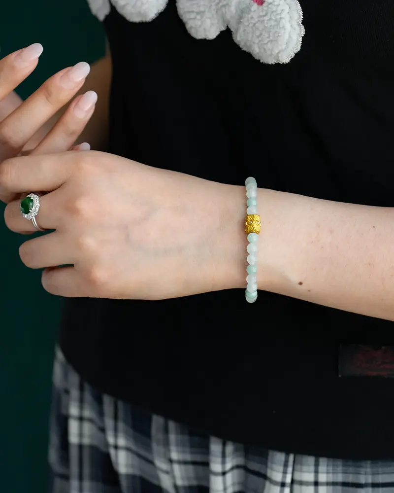 DSC_0655 拷贝 A person wearing a beaded bracelet with a gold accent on their wrist, a silver ring with a green gemstone on a finger, a black shirt, and a plaid skirt.
