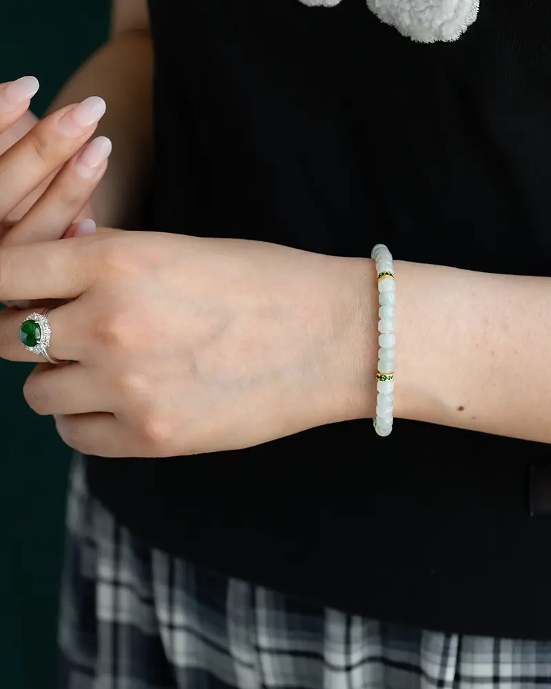 DSC_0660 拷贝 A person wearing a beaded bracelet with gold accents on their wrist and a silver ring with a green stone on their finger, dressed in a black top and plaid skirt.