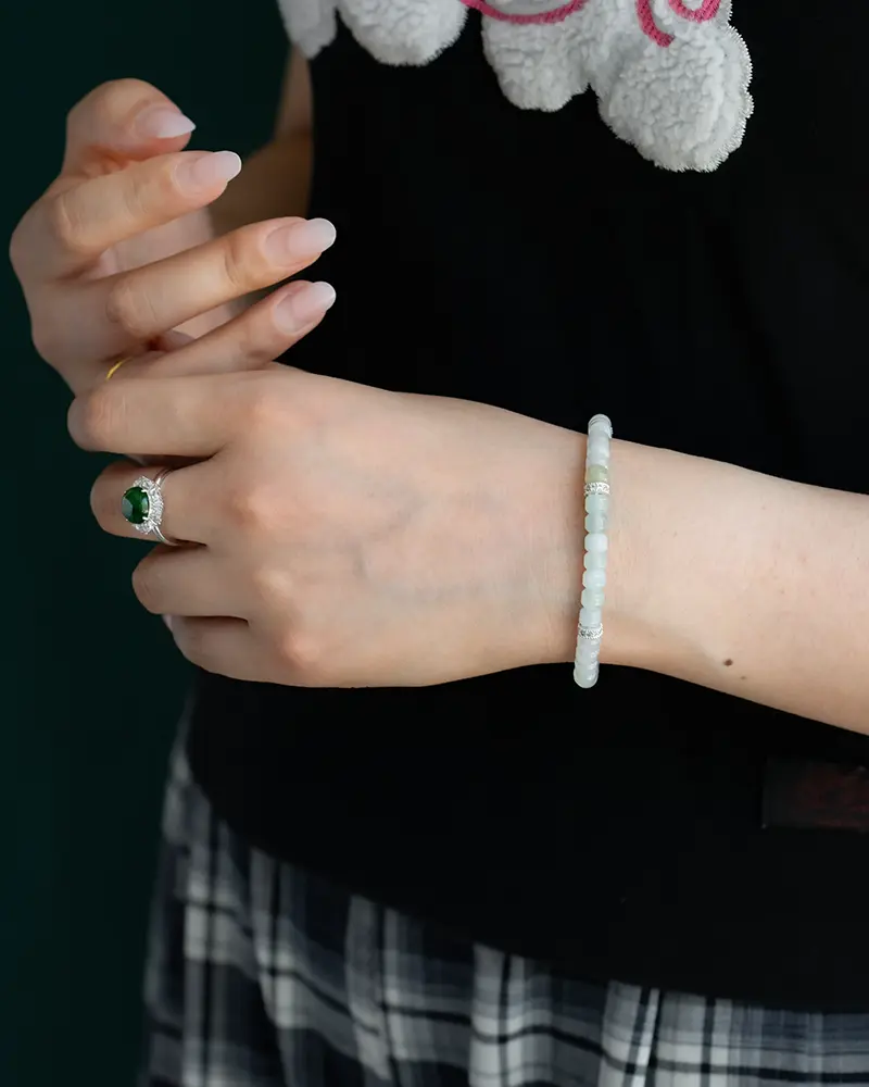 DSC_0667 拷贝 A person wearing a black shirt and plaid skirt displays a delicate beaded bracelet on their wrist and a green gemstone ring on their finger, with neatly manicured nails visible.