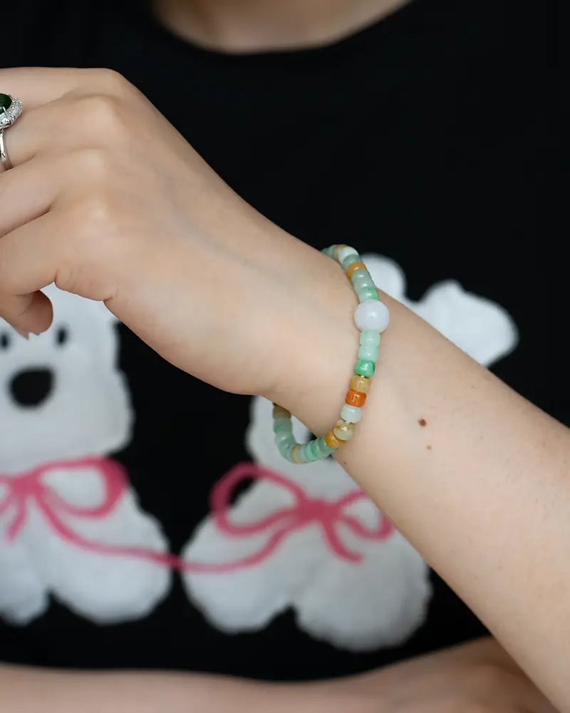 DSC_0704 拷贝 A person wearing a colorful beaded bracelet and a silver ring on their hand, with a black shirt featuring white bear illustrations with pink bows in the background.