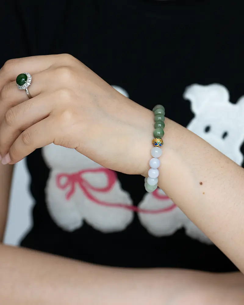 DSC_0709 拷贝 A hand wearing a green gemstone ring and a beaded bracelet with green and pale blue beads, shown against a black shirt with a white dog graphic and pink bow.