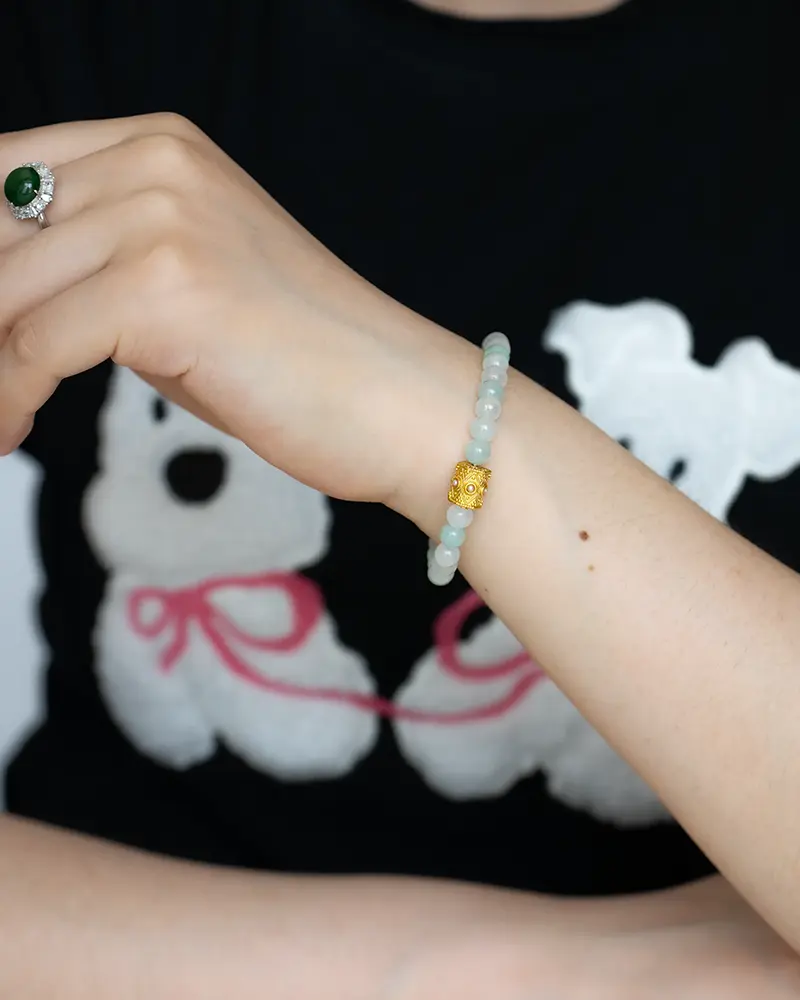 DSC_0717 拷贝 A person wearing a beaded bracelet with a gold accent on their wrist and a green stone ring on their finger. The person is wearing a black shirt with white cartoon bears and pink details.