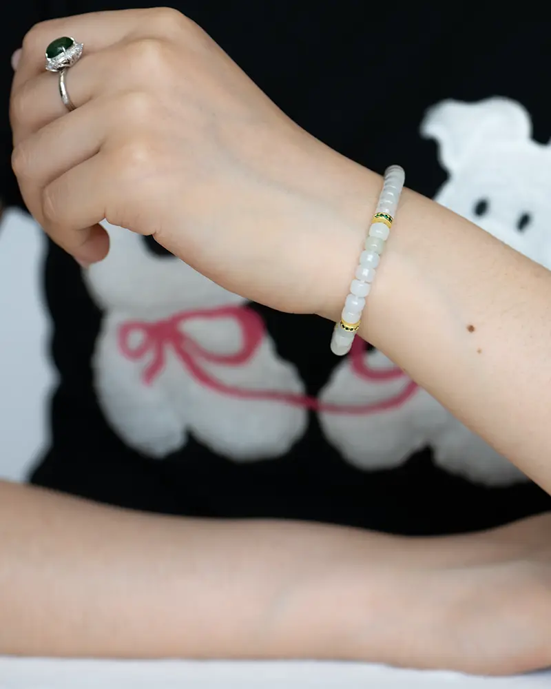 DSC_0725 拷贝 A person wearing a beaded bracelet and a ring rests their arm on a surface. The person is wearing a black shirt with a white bear graphic holding red string.