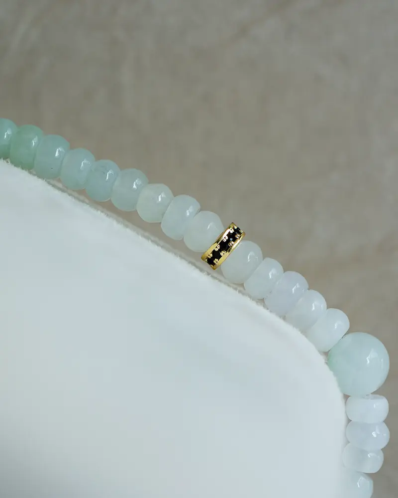 A close-up of a beaded bracelet with pale blue and white round beads and a single gold accent bead on a soft, light-colored surface.