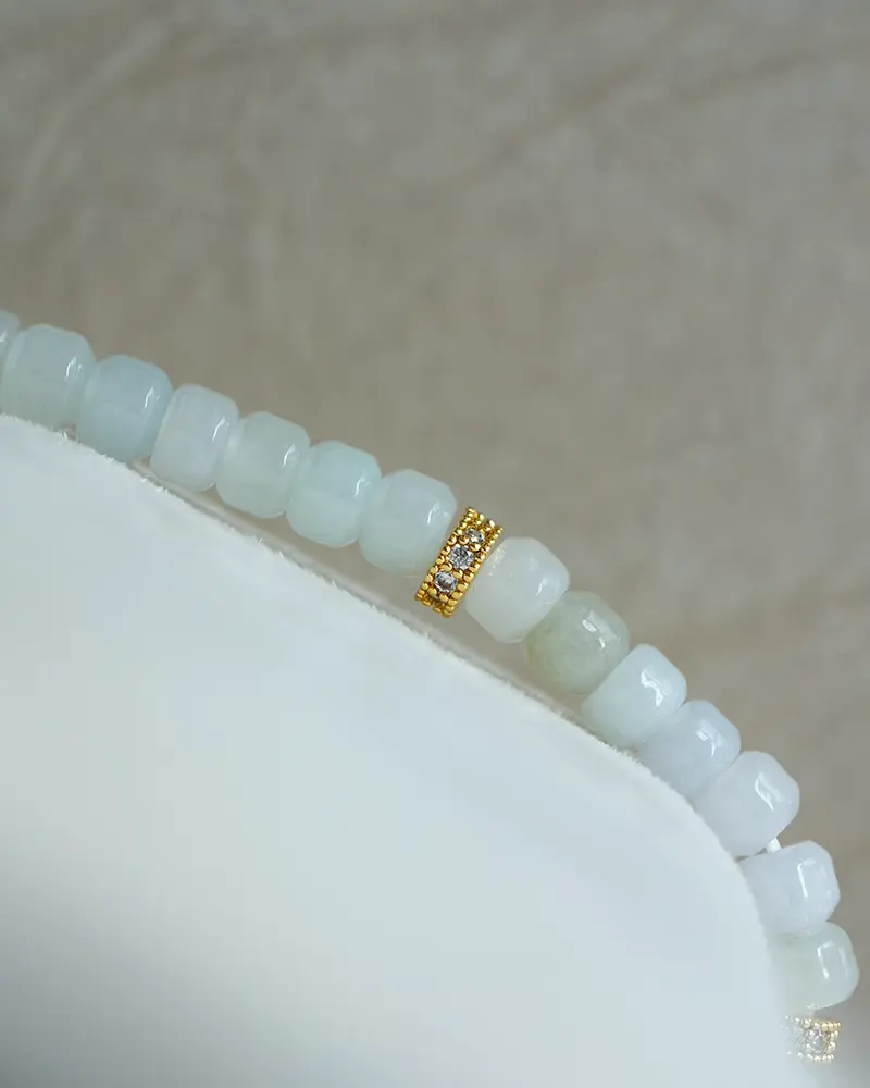 DSC_0736 拷贝 A close-up of a beaded bracelet with pale blue and white rectangular beads, featuring a single gold bead encrusted with small clear stones, displayed on a white surface with a neutral background.
