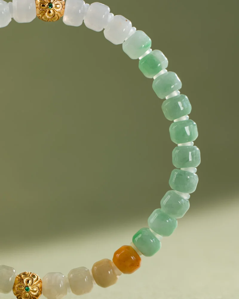 A close-up of the Brownish-Yellow, Light Green and White Jadeite Bracelet—featuring carved beads in light green, white, and brownish-yellow hues with gold-tone accent details—set against a plain background.