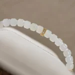 A close-up of the Light Green and White Jadeite Bracelet — Carved Beads with Gold-Tone Accent Details, featuring translucent carved beads and a gold-tone accent, elegantly displayed on a white cushion.
