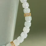 Close-up of a beaded necklace with milky white beads and gold spacers, draped over a light green ceramic cup, evoking the elegance of the Light Green and White Jadeite Bracelet — Carved Beads with Gold-Tone Accent Details.