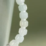 Close-up of the Light Green and White Jadeite Bracelet—carved beads with silver-tone accent details—shown against a muted greenish background.
