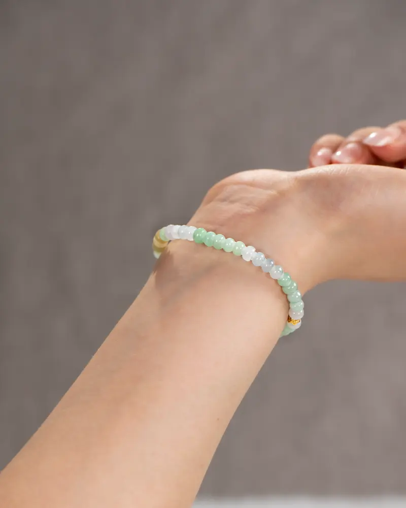 A close-up of a wrist wearing the Brownish-Yellow, Light Green, and White Jadeite Bracelet, featuring ring-shaped beads and gold-tone accent details, shown against a plain neutral background.