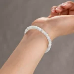 A close-up of a wrist wearing the Light Green and White Jadeite Bracelet, showcasing carved beads in pale, translucent hues with silver-tone accent details against a neutral background.