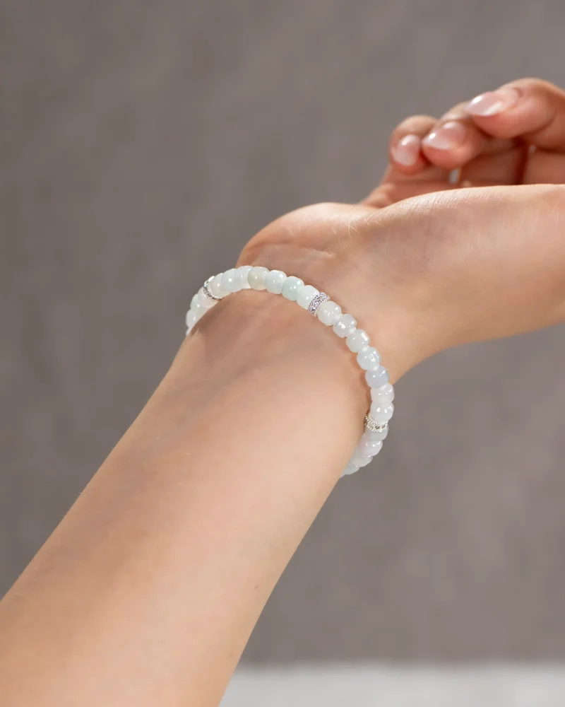 A close-up of a wrist adorned with the Light Green and White Jadeite Bracelet, featuring carved beads in light hues and silver-tone accent details, set against a neutral background.