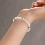 A close-up of a wrist adorned with the Light Green and White Jadeite Bracelet—carved beads and gold-tone spacer details—set against a softly blurred, neutral background.