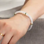A close-up of a wrist wearing the Light Green and White Jadeite Bracelet—carved beads with gold-tone spacer details. The person also has a gold ring on their finger.