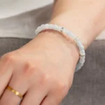 A close-up of a wrist wearing the Light Green and White Jadeite Bracelet—featuring carved beads and silver-tone accents—paired with a simple gold ring.