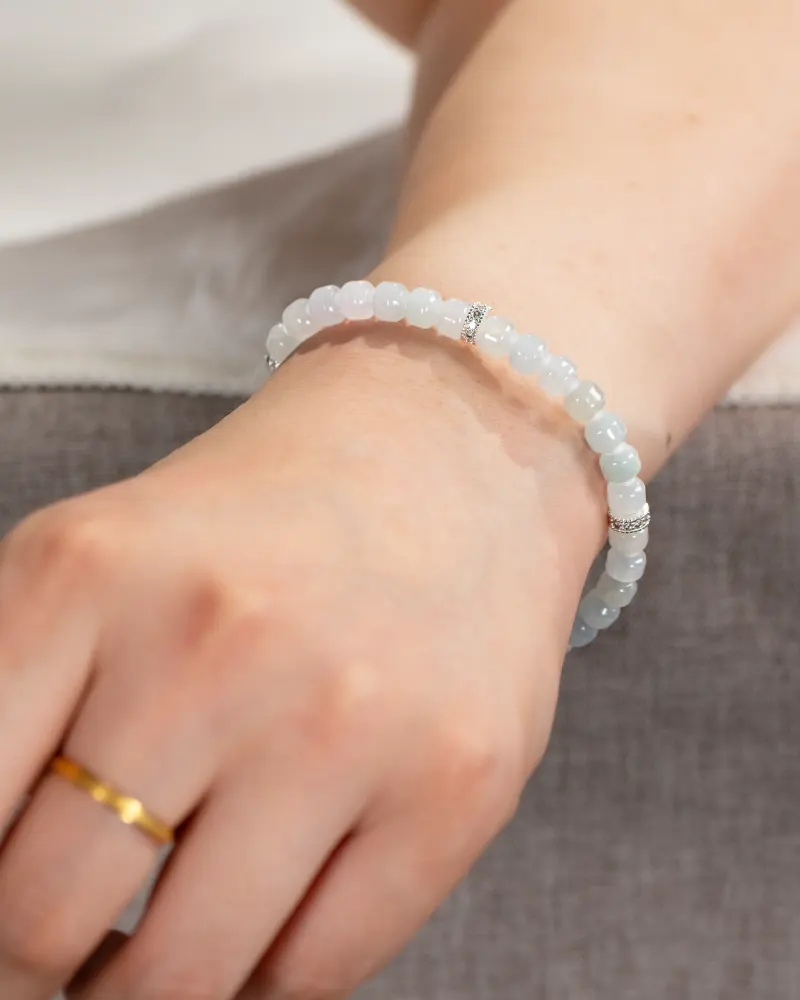 DSC_1178 拷贝 A close-up of a wrist wearing the Light Green and White Jadeite Bracelet—featuring carved beads and silver-tone accents—paired with a simple gold ring.