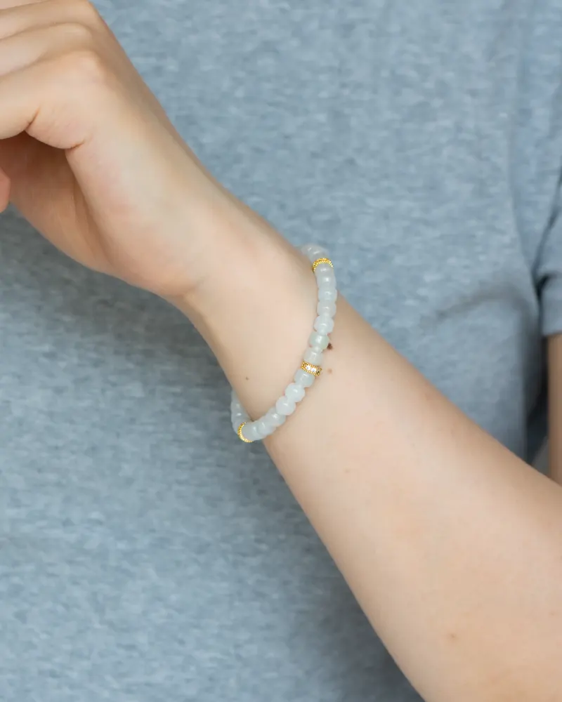 DSC_1181 拷贝 A person in a grey t-shirt wears the Light Green and White Jadeite Bracelet—featuring carved beads and gold-tone accent details—on their wrist.