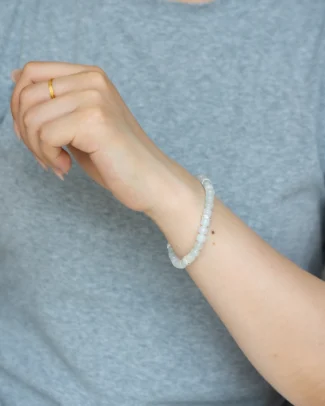 A person wearing a gray shirt displays the Light Green and White Jadeite Bracelet — featuring carved beads with silver-tone accent details — on their wrist, along with a simple gold ring on their finger.