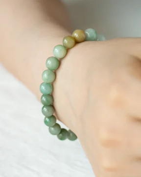 A close-up of a wrist adorned with the Light Green, Light Purple, and Brownish Yellow Jadeite Bead Bracelet featuring spherical beads and gold-tone accent detail, set against a soft, neutral background.