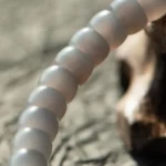 A close-up of a translucent, grayish beaded bracelet or string of beads on a textured surface, with soft lighting creating a gentle, blurred background.