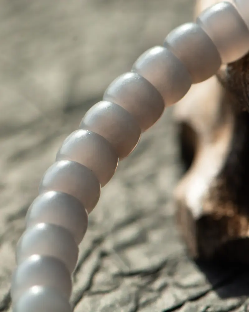 LYU_4035 拷贝 A close-up of a translucent, grayish beaded bracelet or string of beads on a textured surface, with soft lighting creating a gentle, blurred background.