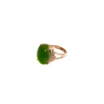 A gold ring featuring a large oval green gemstone and small round accent diamonds on the band, displayed on a white background.